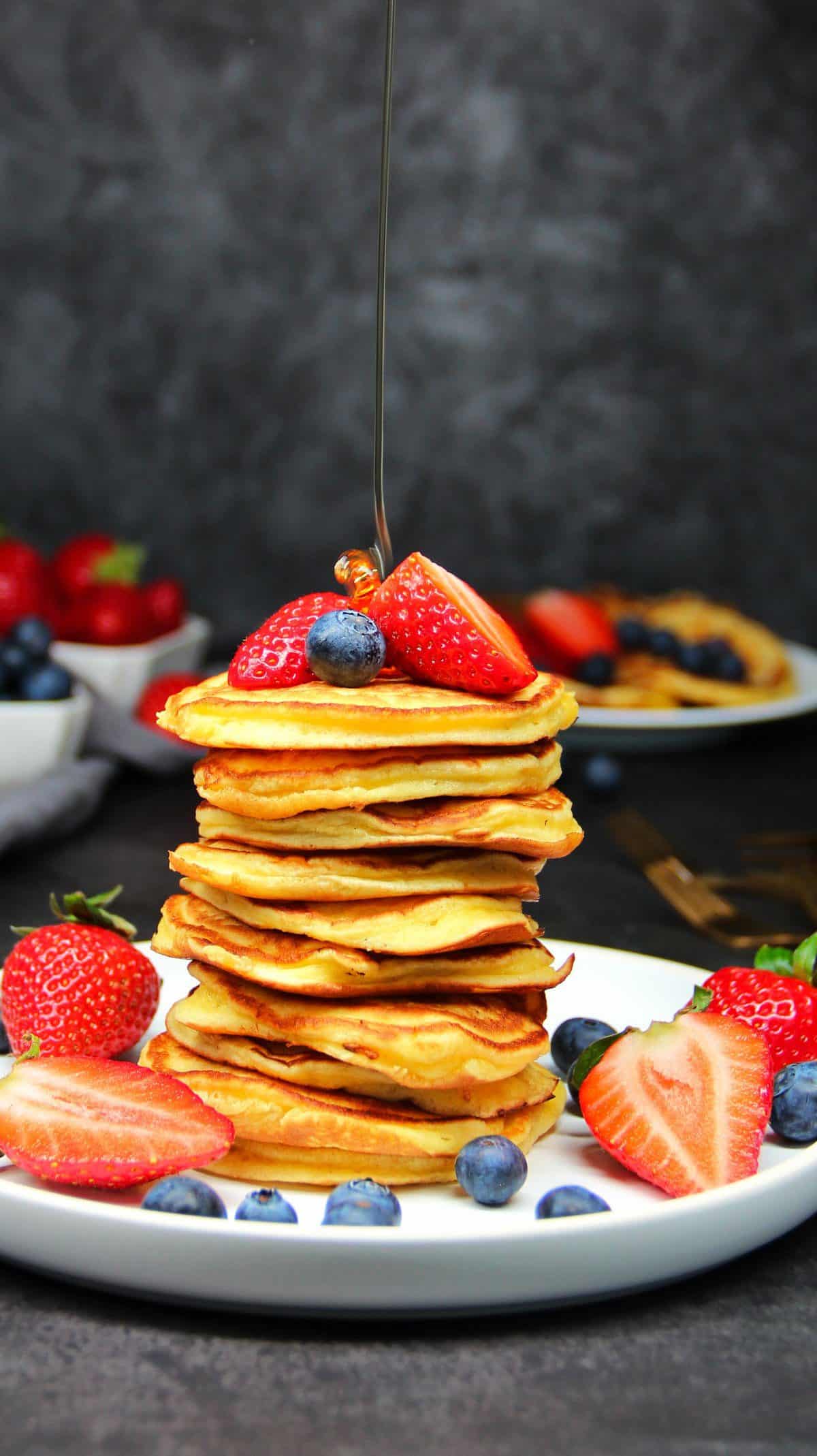 Pancakes, auf einem Teller gestapelt, mit frischen Beeren und Ahornsirup