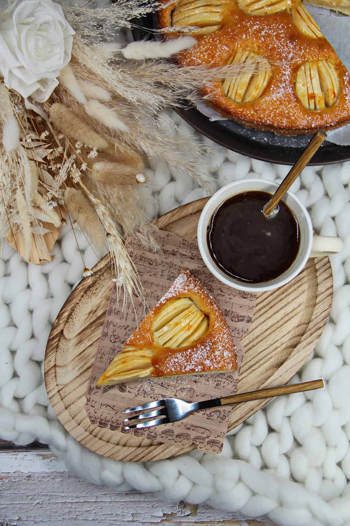 Versunkener Apfelkuchen, Kuchenstück mit einer Tasse Kaffee auf einem kleinen Holz-Servierbrett