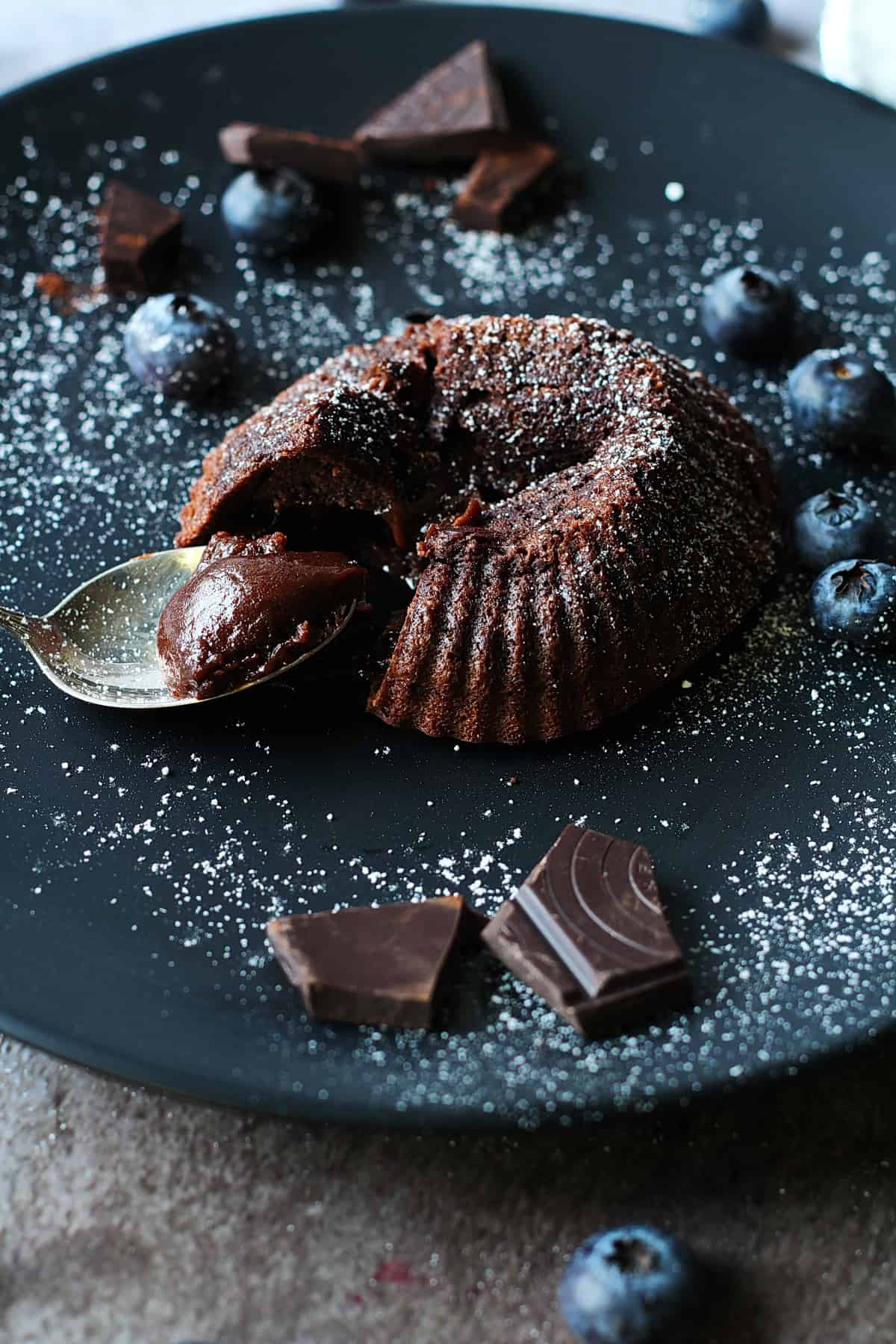 Lava Cake, Muffin auf einem schwarzen Teller mit Puderzucker und Blaubeeren