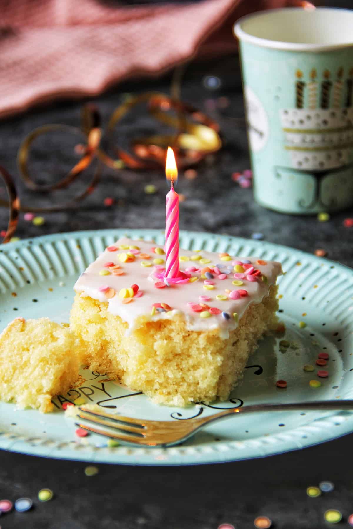 Konfetti-Kuchen vom Blech, Kuchenstück mit einer pinken Kerze auf einem Geburtstagsteller