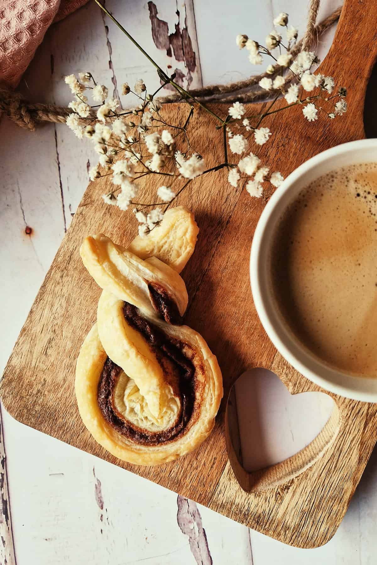 Blätterteig-Hasen mit Nutella, auf einem Holzbrett neben einer Kaffeetasse und Schleierkraut