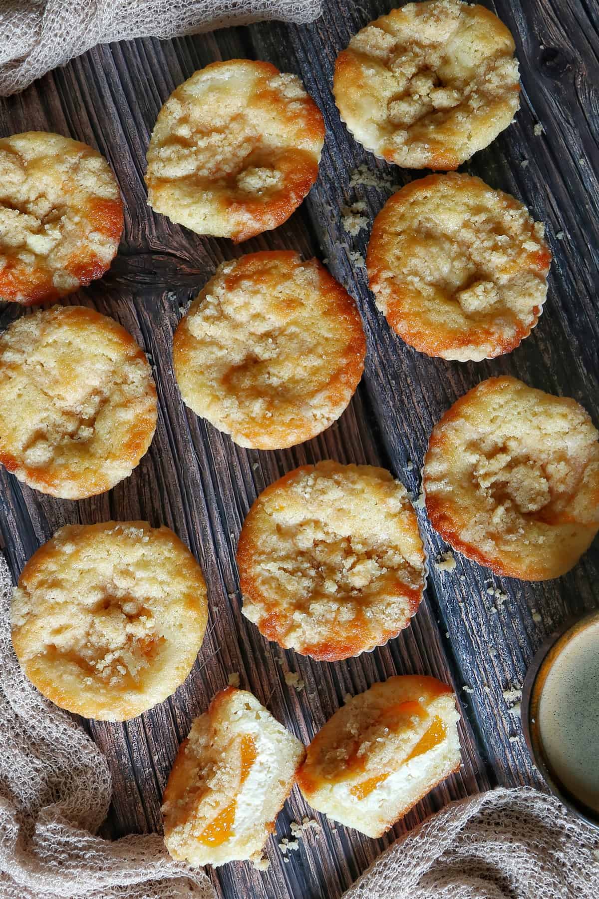 Mandarinen-Muffins mit Frischkäse und Streuseln auf einem dunklen Holztisch.