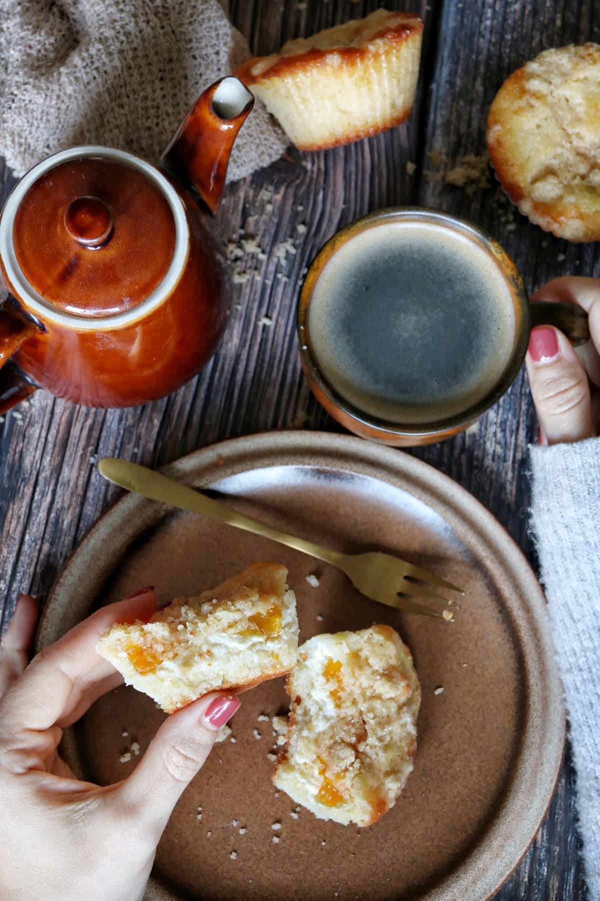 Mandarinen-Muffins mit Frischkäse und Streuseln auf einem Teller. Ebenfalls auf dem Tisch: eine Tasse Kaffee und eine Kaffeekanne.