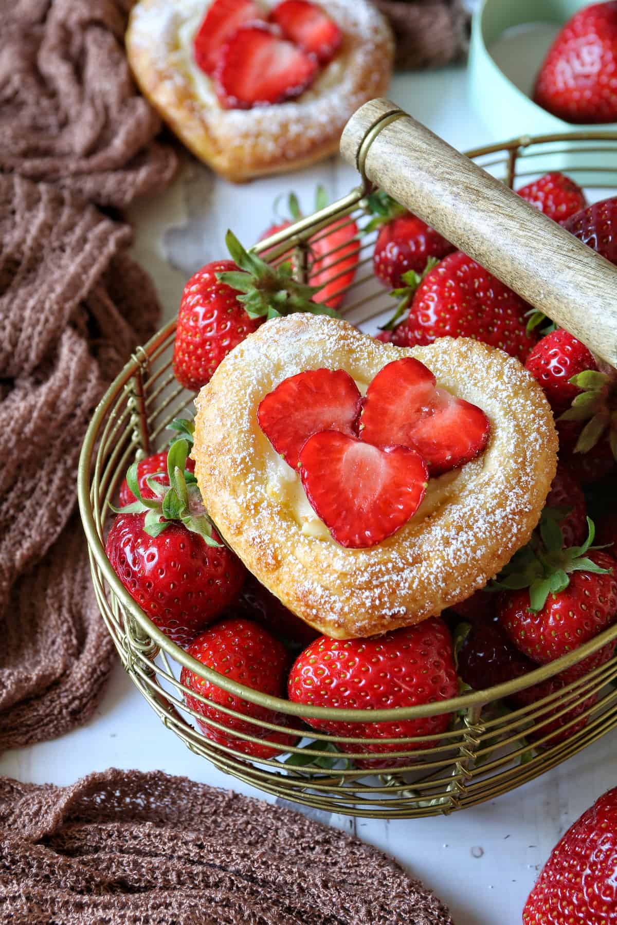 Blätterteig-Herzen mit Erdbeeren in einem goldenen Drahtkorb voller Erdbeeren