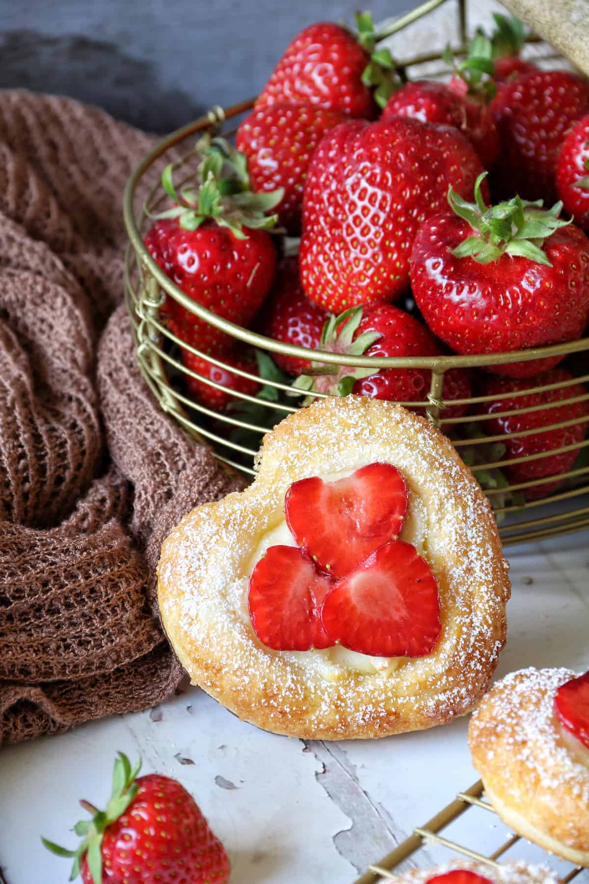 Blätterteig-Herzen mit Erdbeeren an einen Korb voller frischer Erdbeeren gelehnt