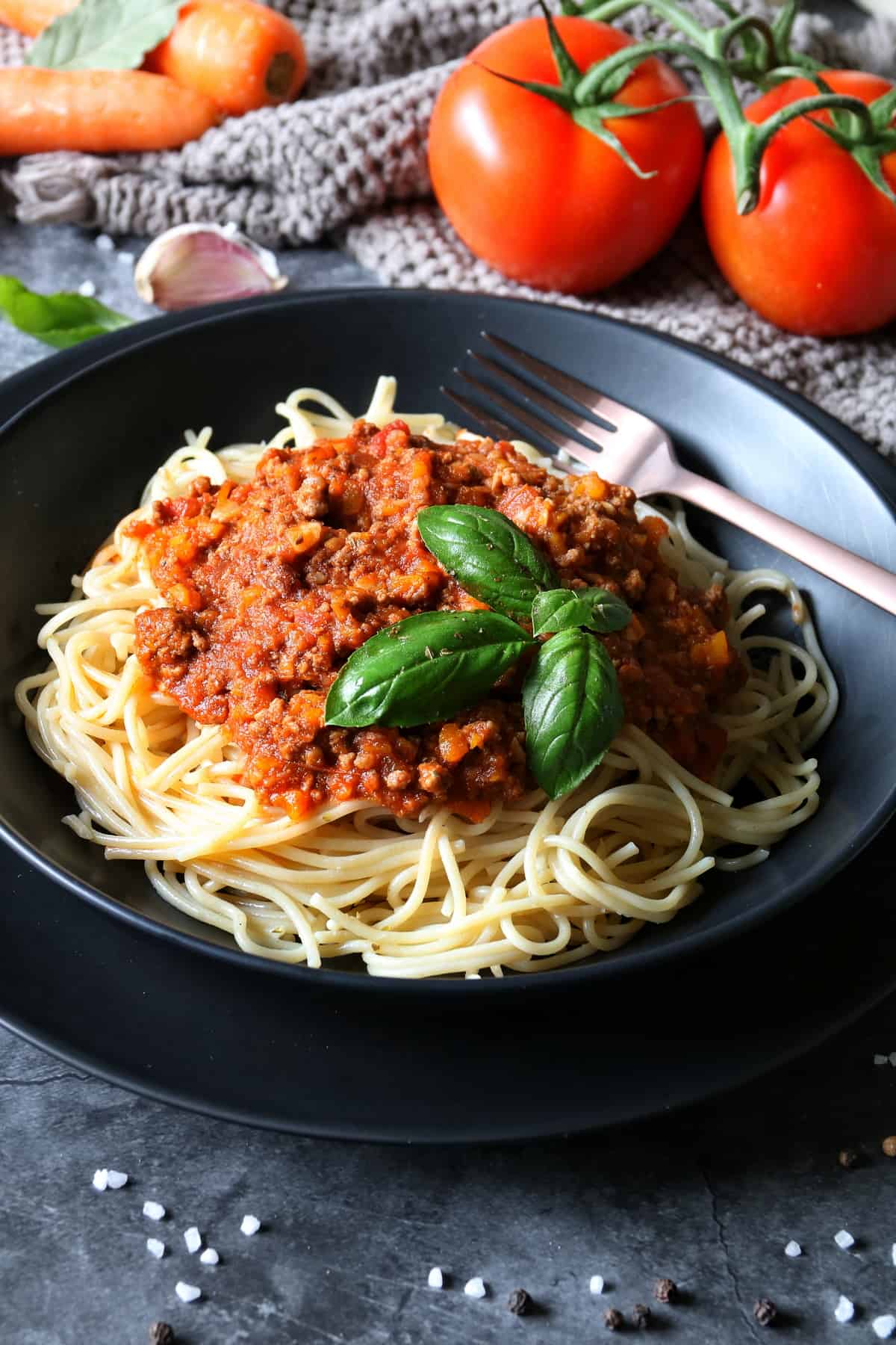 Spaghetti Bolognese aus dem Thermomix® in einem tiefen, schwarzen Teller, mit Basilikum garniert. Im Teller liegt eine Gabel.