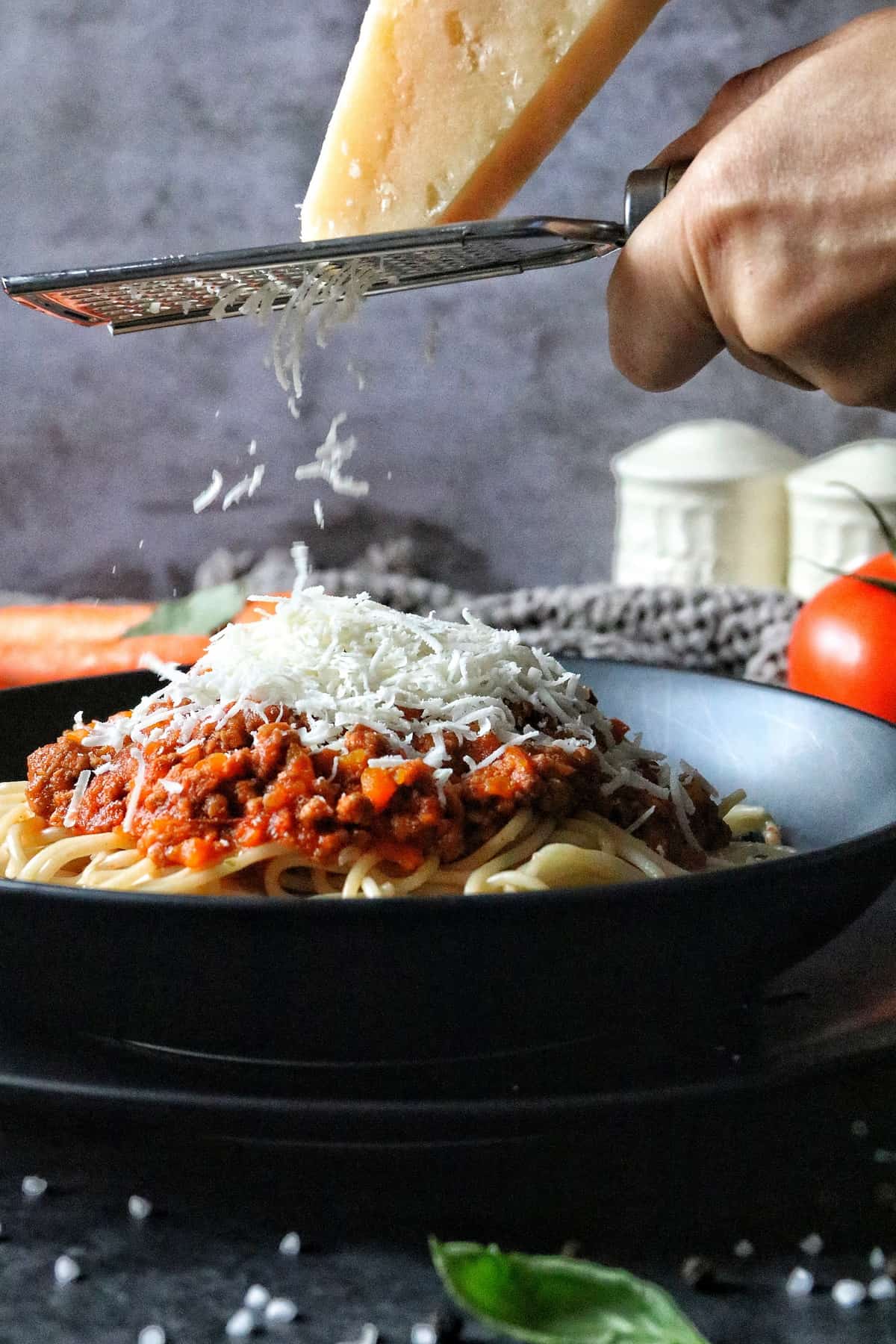 Spaghetti Bolognese in einem Teller, während von oben Parmesan darüber gerieben wird. 