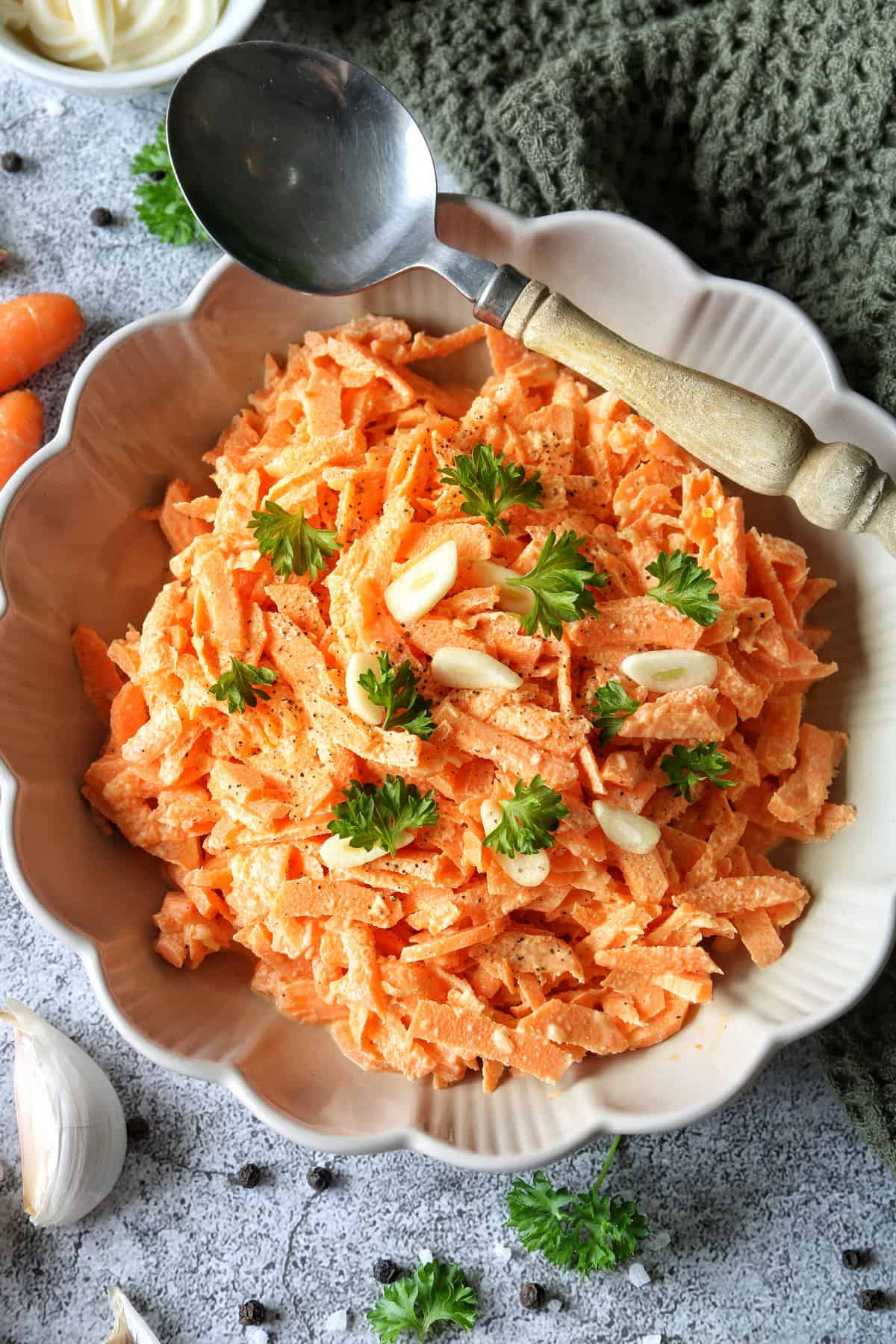 Einfacher Karottensalat mit Schmand und Mayonnaise in einem Teller mit Wellenrand. Quer über dem Teller liegt ein Holzlöffel.