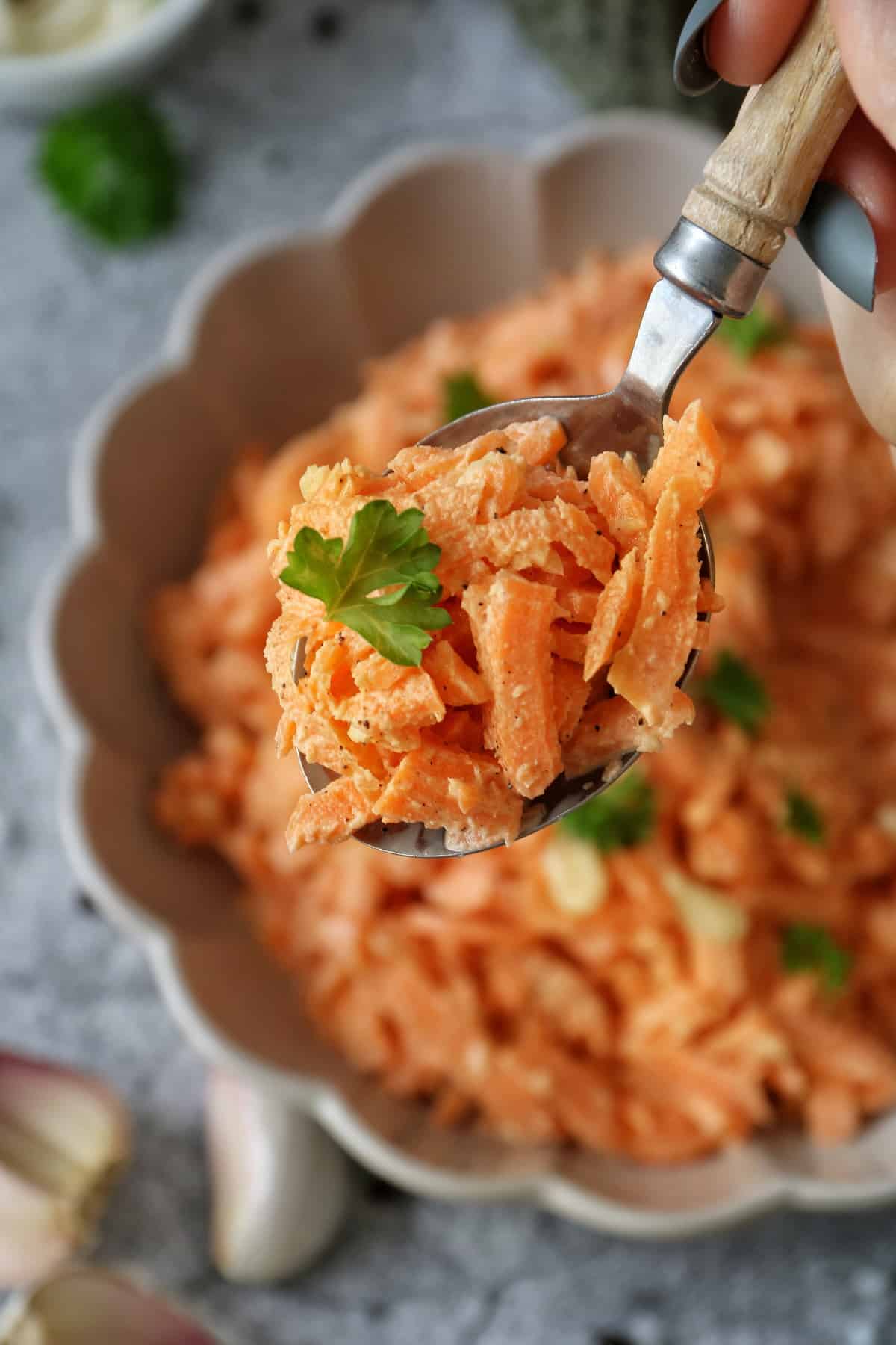 Einfacher Karottensalat mit Schmand und Mayonnaise in einem Teller mit Wellenrand. Ein Löffel mit dem Salat ist in der Schärfe.