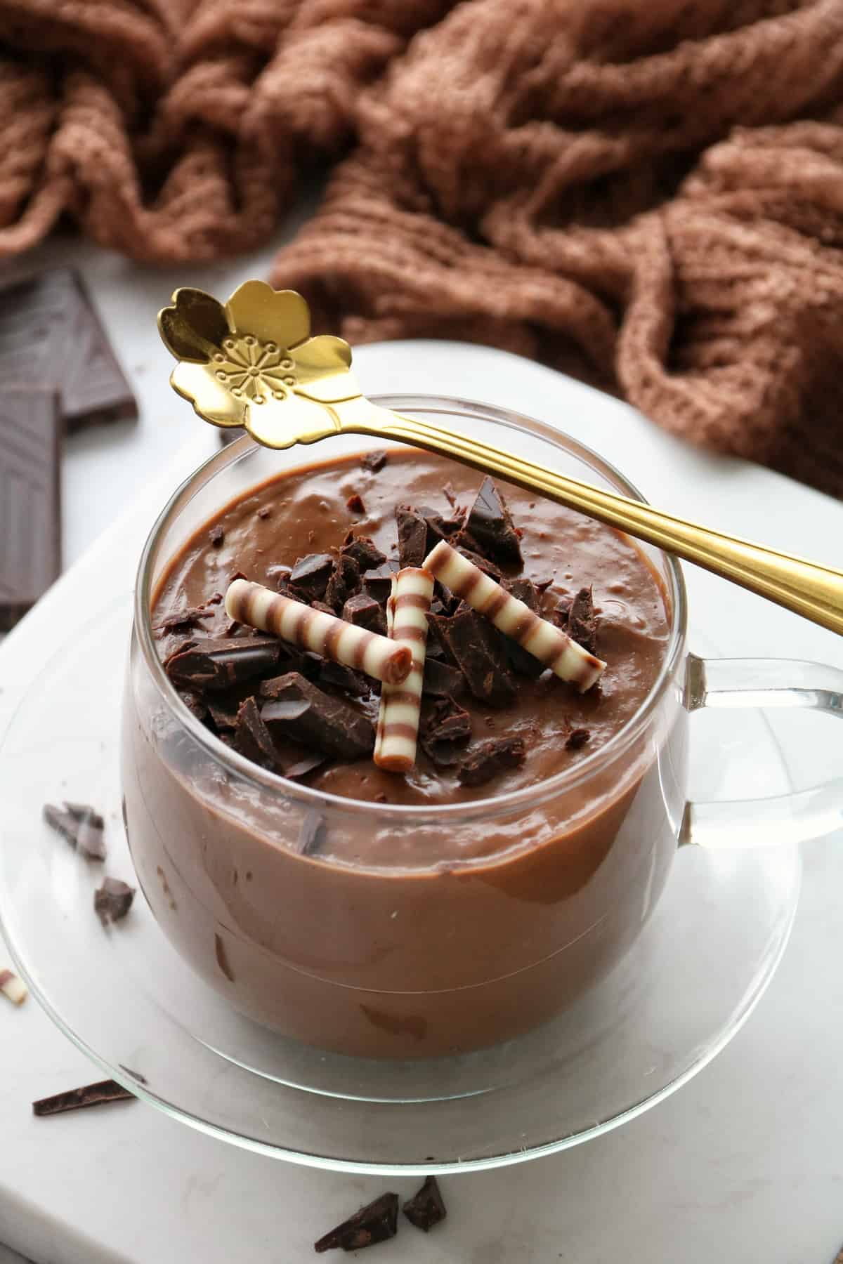 Schokoladenpudding im Thermomix® in einem Glas mit Schokostückchen und Zebraröllchen dekoriert. Ein goldener Löffel liegt quer über dem Glas