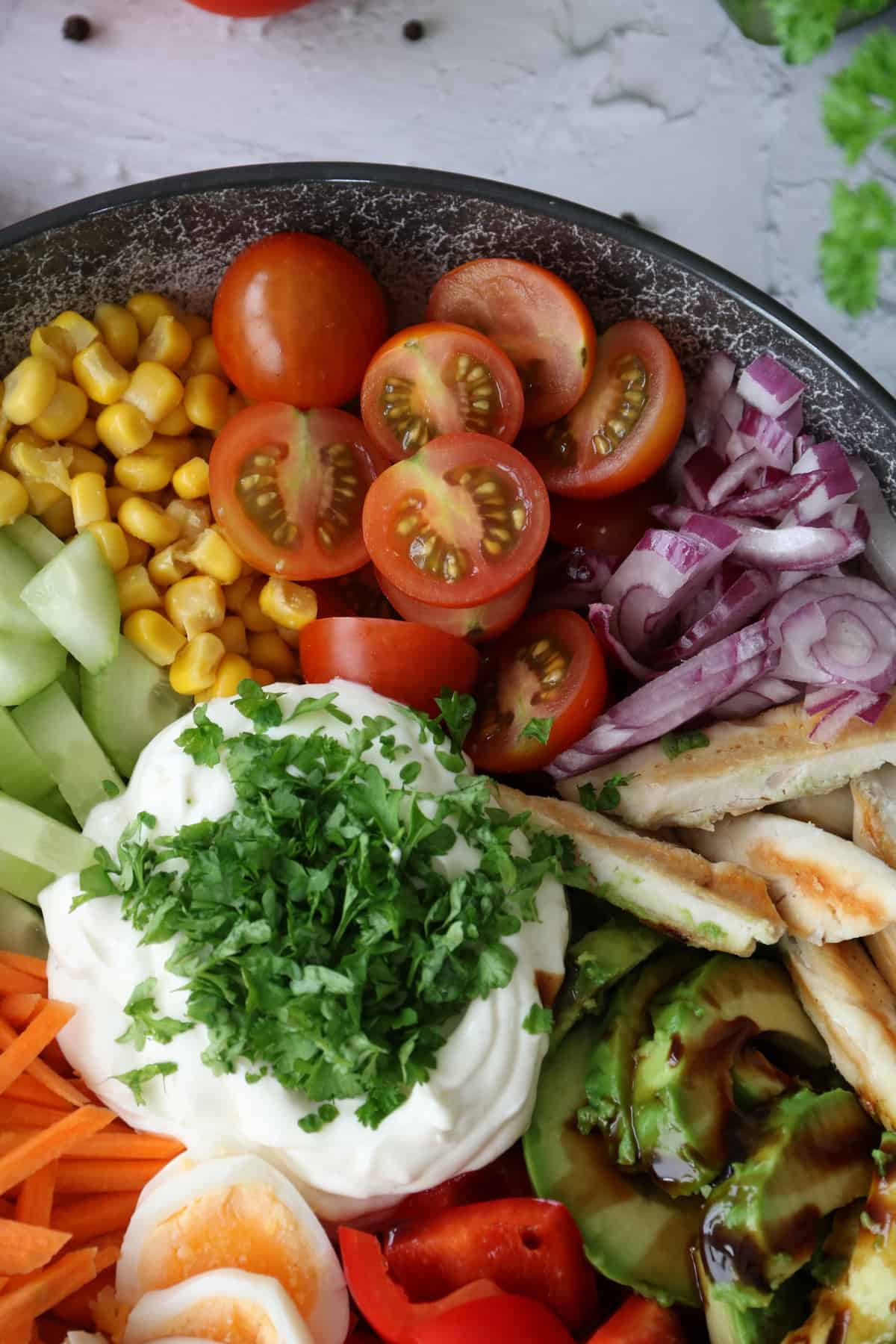 Bunte Salat Bowl mit Avocado, Hähnchen und Knoblauchdressing in einer Schüssel angerichtet. Nahaufnahme der Tomaten, Zwiebeln, Hähnchenstreifen und vom Dressing.