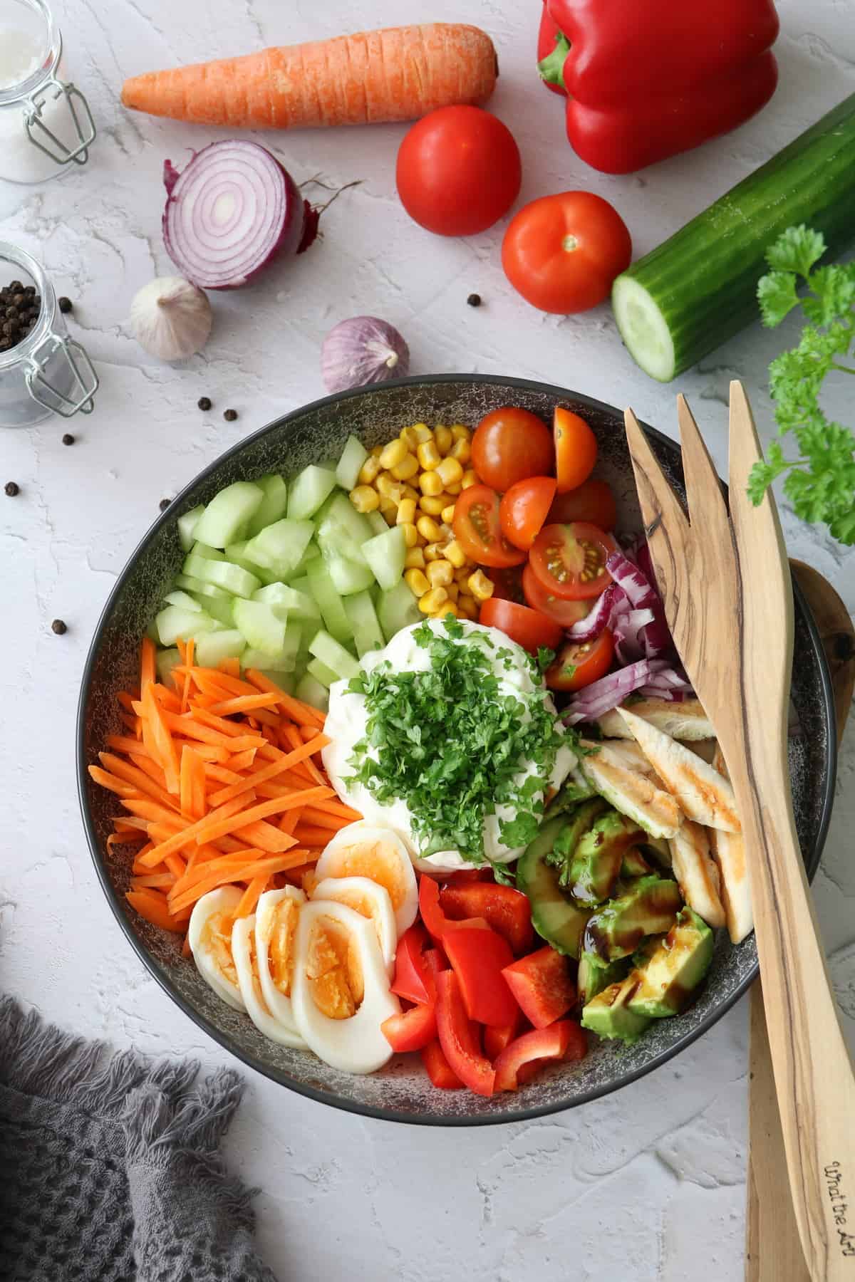 Bunte Salat Bowl mit Avocado, Hähnchen und Knoblauchdressing in einer Schüssel angerichtet. Darauf Salatbesteck aus Holz.