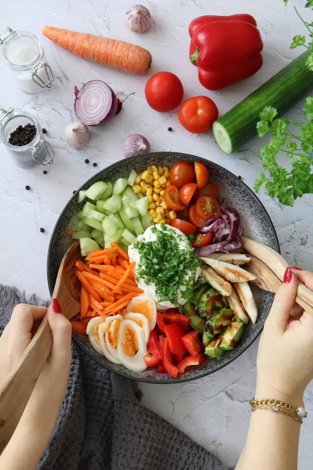 Bunte Salat Bowl mit Avocado, Hähnchen und Knoblauchdressing in einer Schüssel angerichtet beim Durchmischen mit Salatbesteck aus Holz.