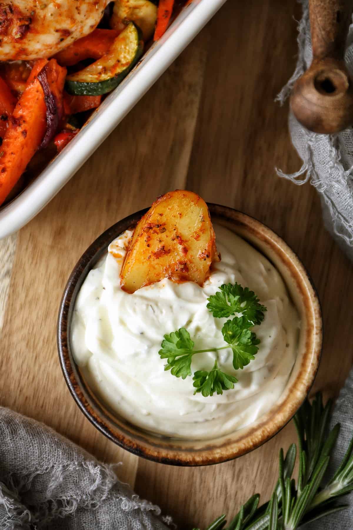 Ofenhähnchen mit mediterranem Gemüse, eine Kartoffel ist in ein Schälchen mit Sour Cream getaucht