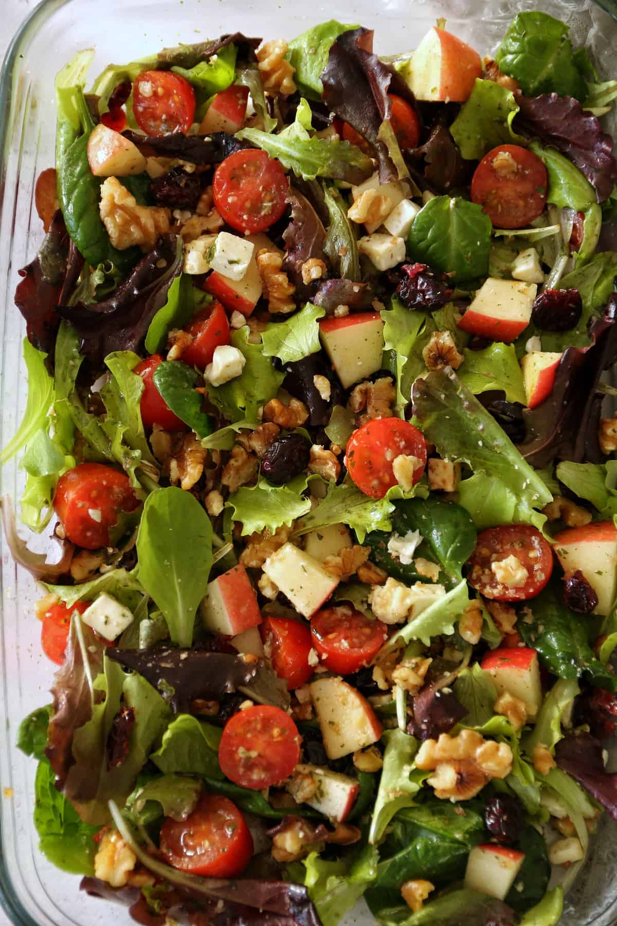 Nahaufnahme vom frischen Salat mit dem würzigen Knoblauchdressing, das die Äpfel, Salatblätter, den Feta und die Tomaten umhüllt.
