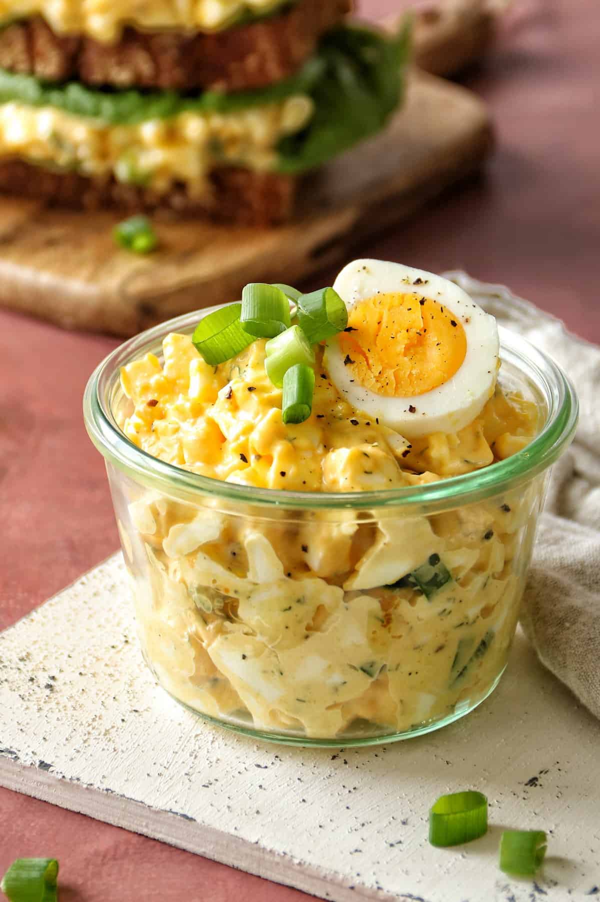 Der beste Eiersalat ist in ein Weck-Glas gefüllt. Er ist mit einem halben aufgeschnittenen Ei, Frühlingszwiebeln und frisch gemahlenem Pfeffer garniert.