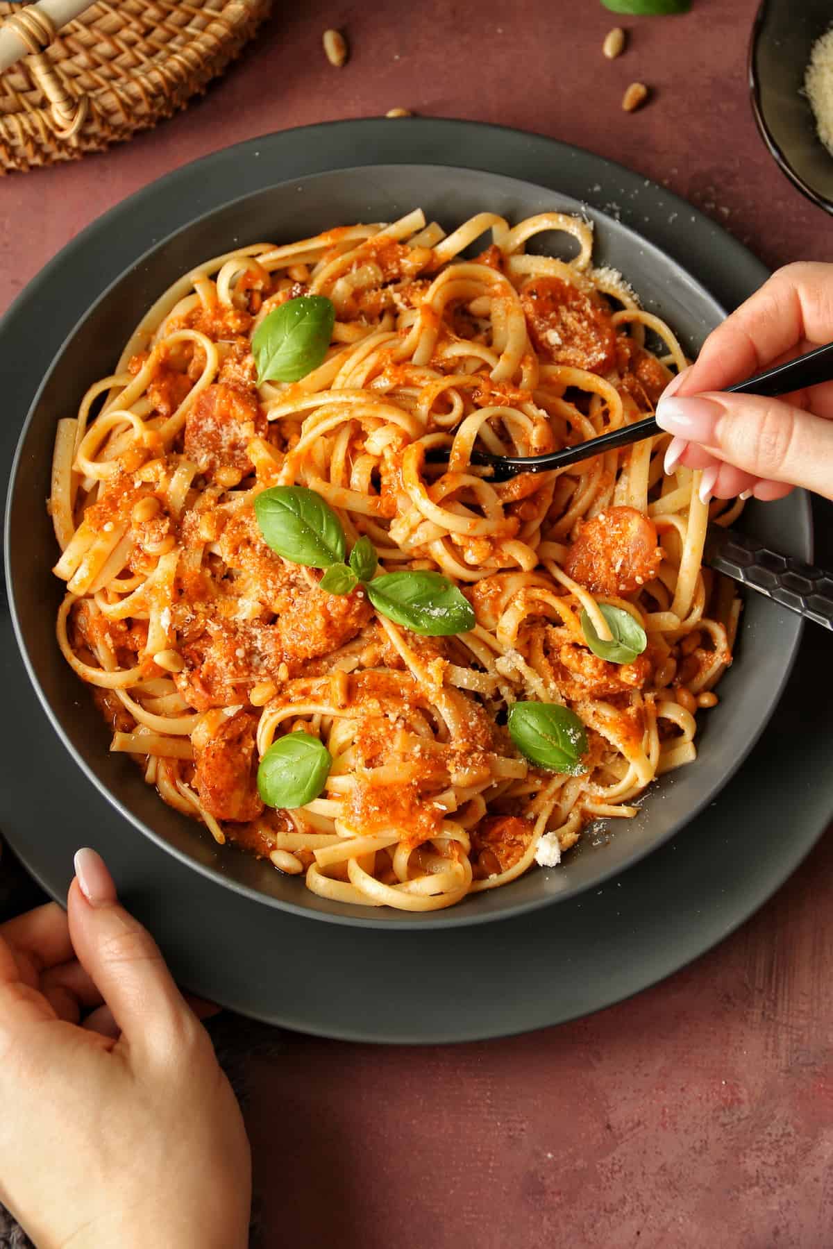 Pasta mit Pesto Rosso in einem dunkelgrauen Teller. Außerdem sind 2 Hände im Bild. Die eine hält die Gabel und die andere hält den Teller fest.