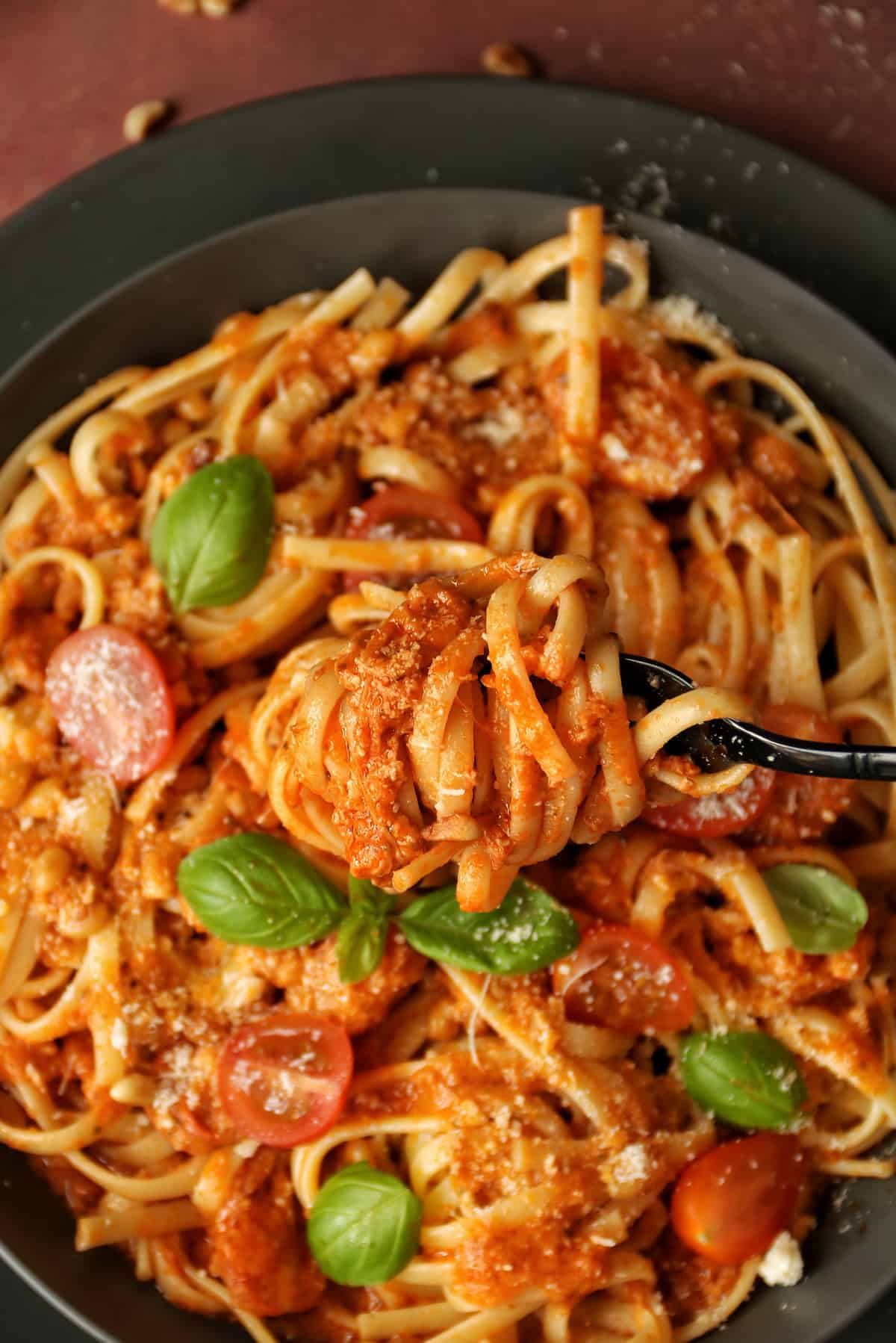 Pasta mit Pesto Rosso, mit Cherrytomaten, Parmesan, Mozzarella und Basilikumblättern. Die Linguine sind um eine Gabel gewickelt.