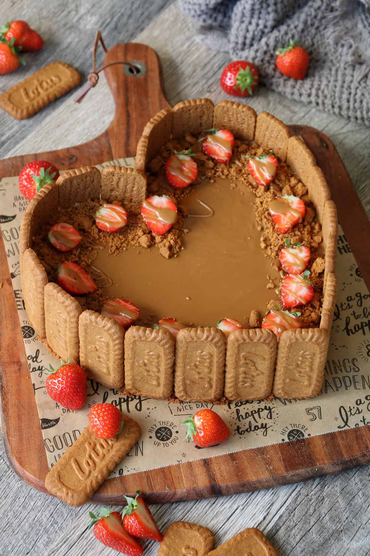 Lotus Cheesecake in einer Herzform mit frischen Erdbeeren auf einem Holztisch