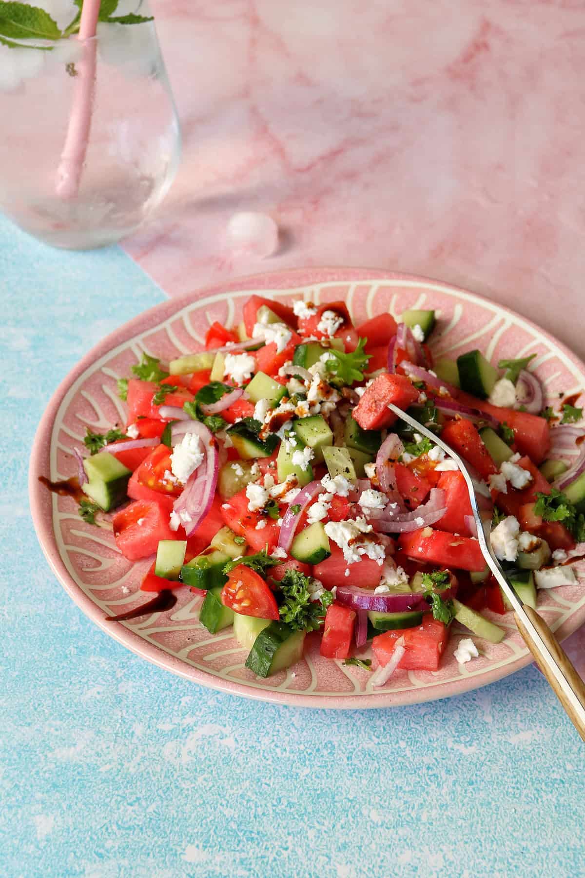 Wassermelonensalat mit Feta, Gurken und Tomaten auf einem rosafarbenen Teller