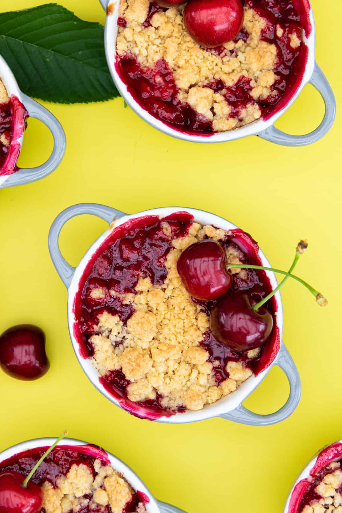 Kirsch-Crumble auf einem gelben Hintergrund. Getoppt mit 2 Kirschen.