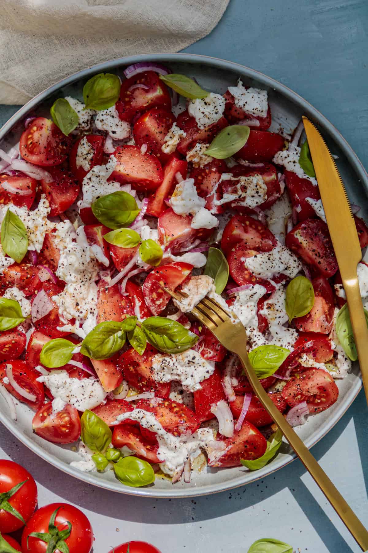 Eine Gabel liegt auf dem Salatteller und hat eine Tomate sowie ein Stück Burrata aufgespießt. 