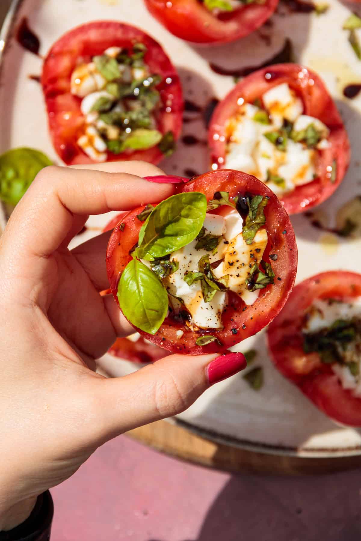 Eine Hand hält eine gefüllte Tomatenhälfte. Dekoriert ist die Tomate mit frischen Basilikumblättern.