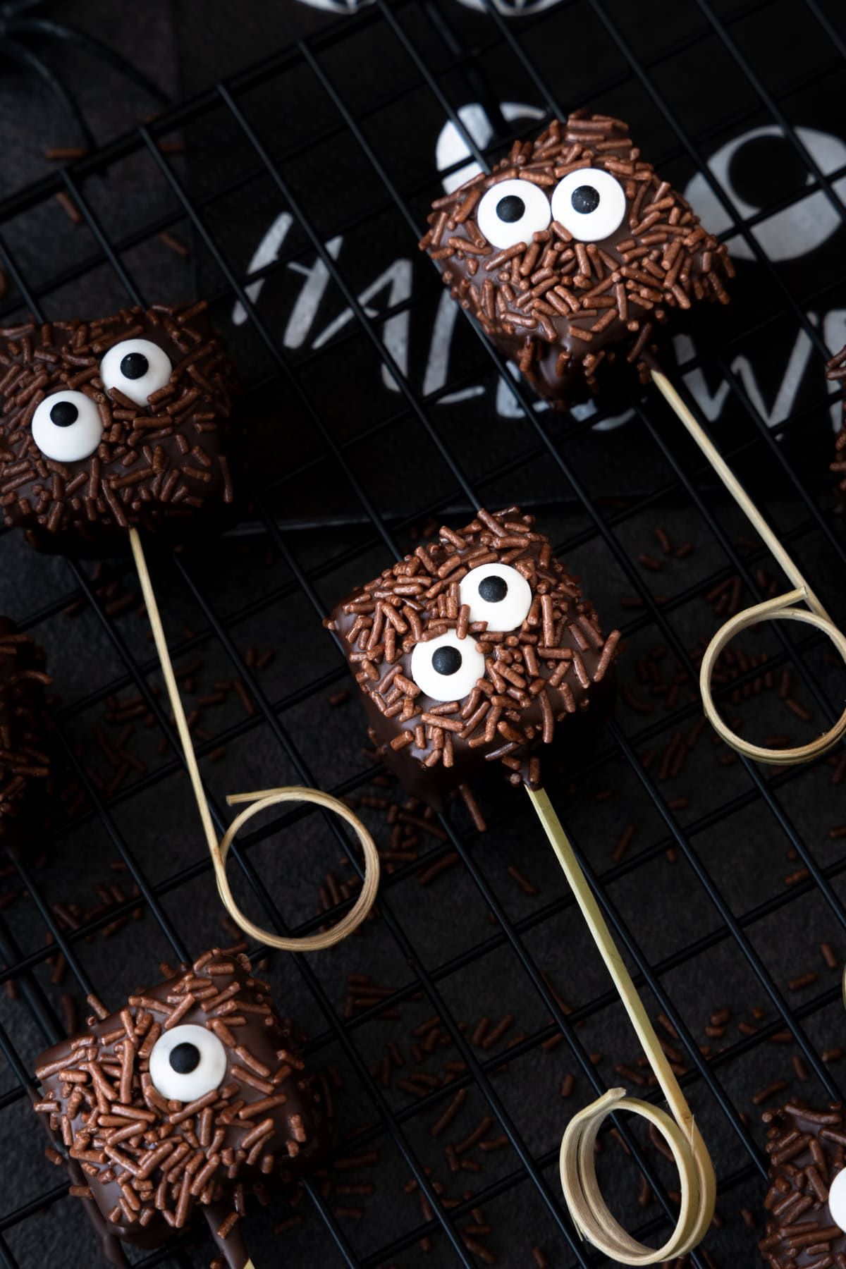 Halloween-Monster-Brownies auf einem schwarzen Gitter. Im Hintergrund liegt eine Halloween Serviette.