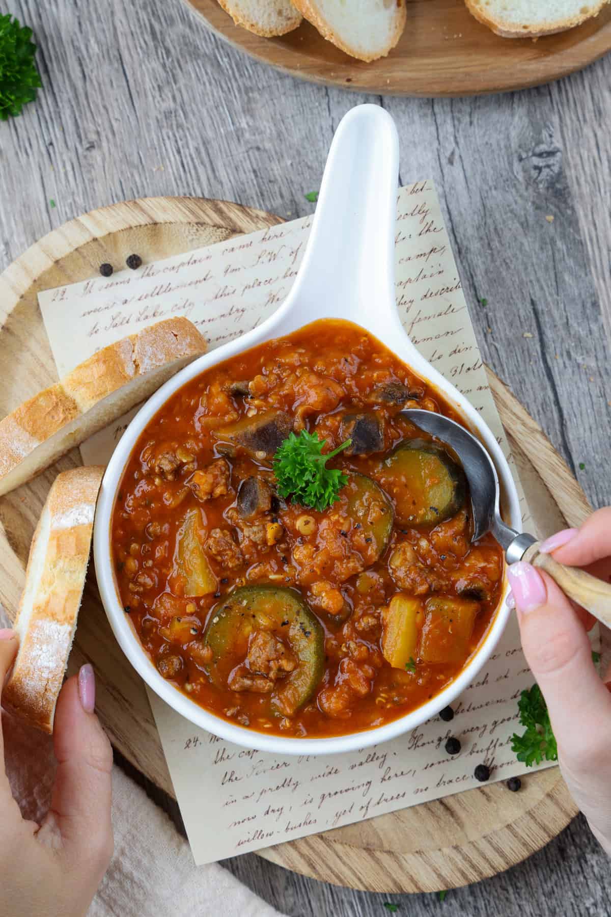 Deftiger Gemüse-Linsen-Eintopf mit Hackfleisch aus dem Thermomix® in einer weißen Servierschüssel. Es ist eine Hand zu sehen, die einen Löffel in den Eintopf taucht.