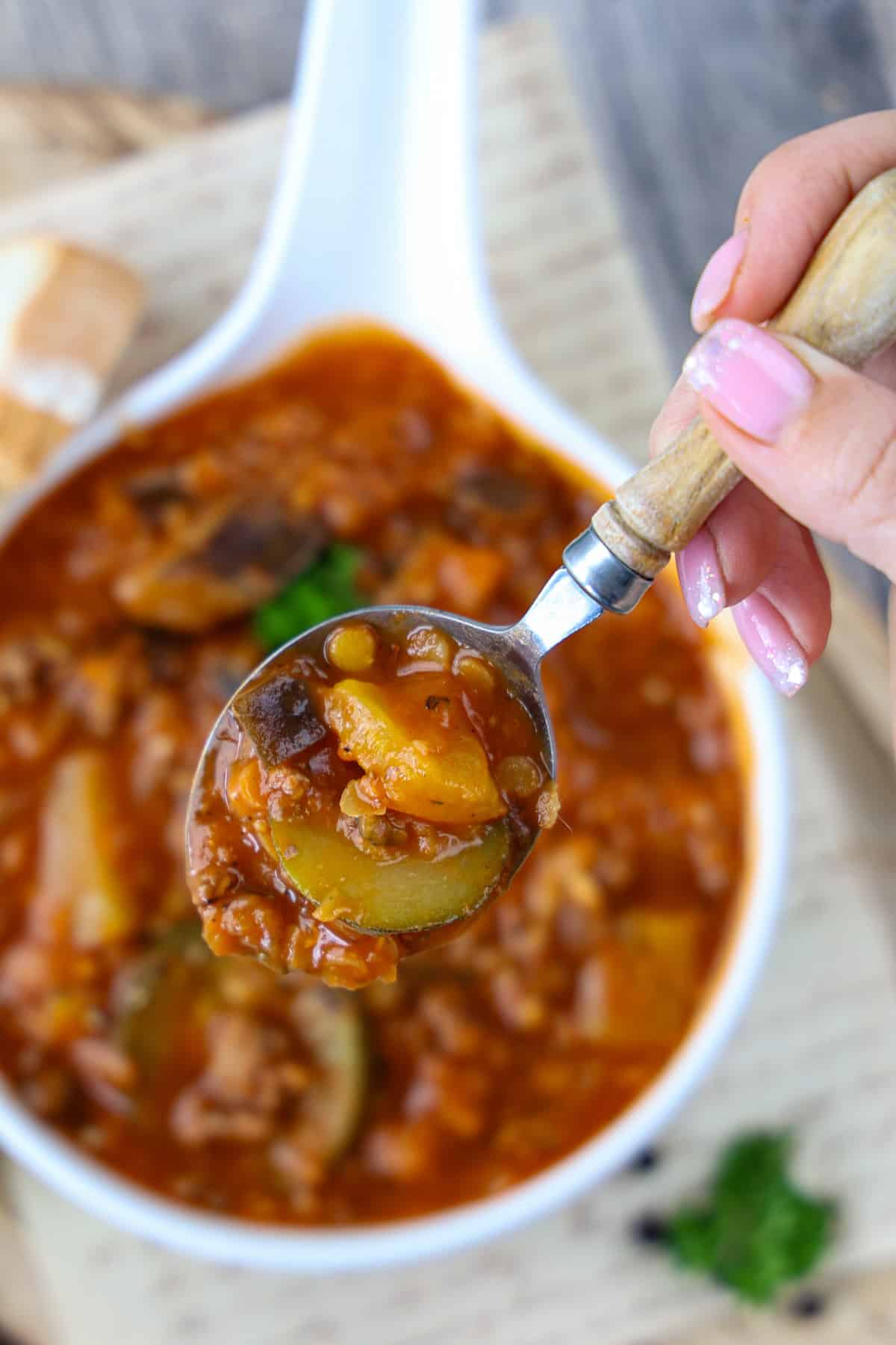 Gemüse-Linsen-Eintopf mit Hackfleisch wird auf einem Löffel in die Kamera gehalten. Zu erkennen ist das Gemüse, d.h. Zucchini, Aubergine und Paprika.