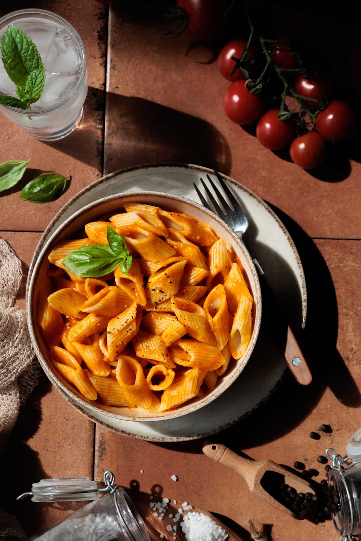 Tomatensoße aus frischen, ofengerösteten Tomaten mit Nudeln vermengt in einem tiefen Teller. Mit frisch gemahlenem Pfeffer und Basilikumblättern garniert.