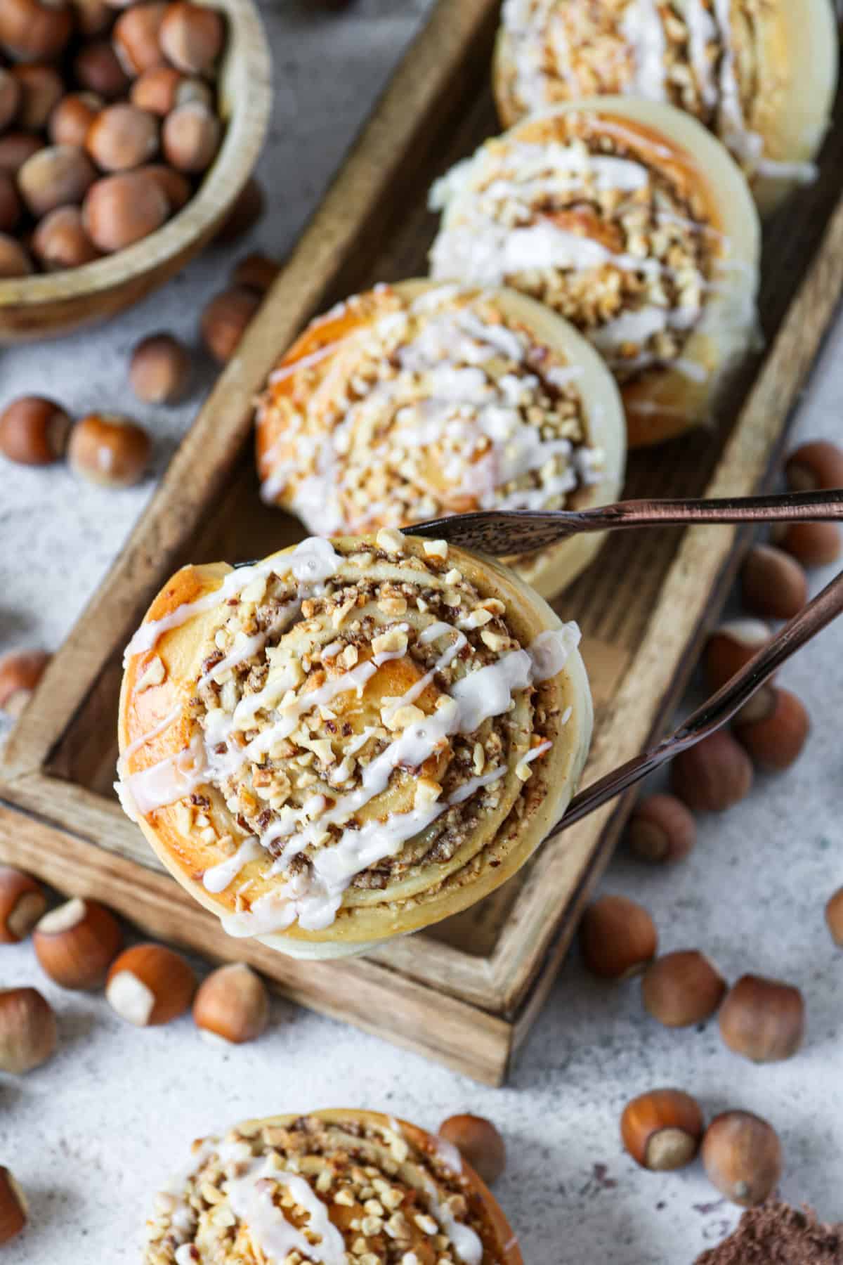 Eine saftige Nuss-Schnecke, mit Puderzuckerguss garniert, wird mit einer Gebäckzange in die Kamera gehalten.