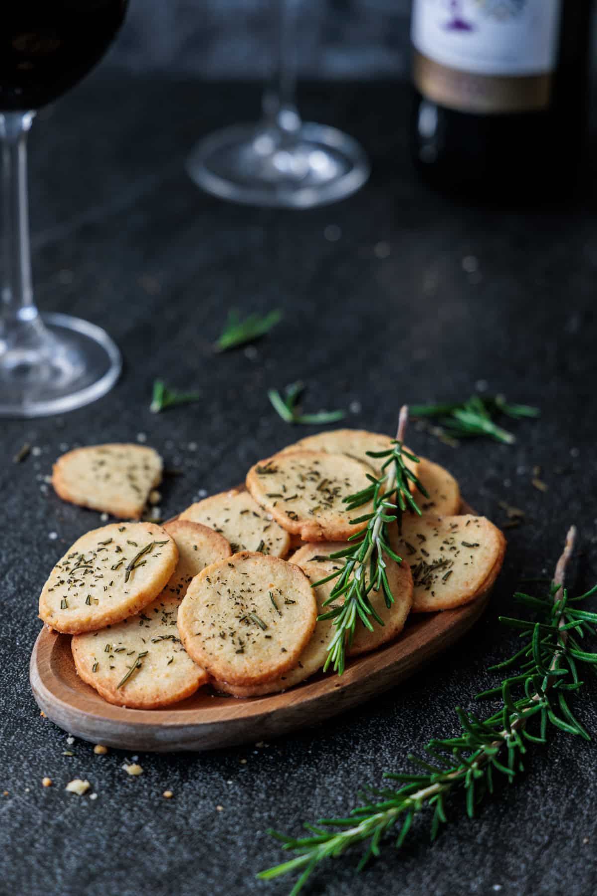 Parmesan-Rosmarin-Cracker (Kekse) auf einem kleinen Holz-Tablett mit frischen Rosmarin-Zweigen daneben.