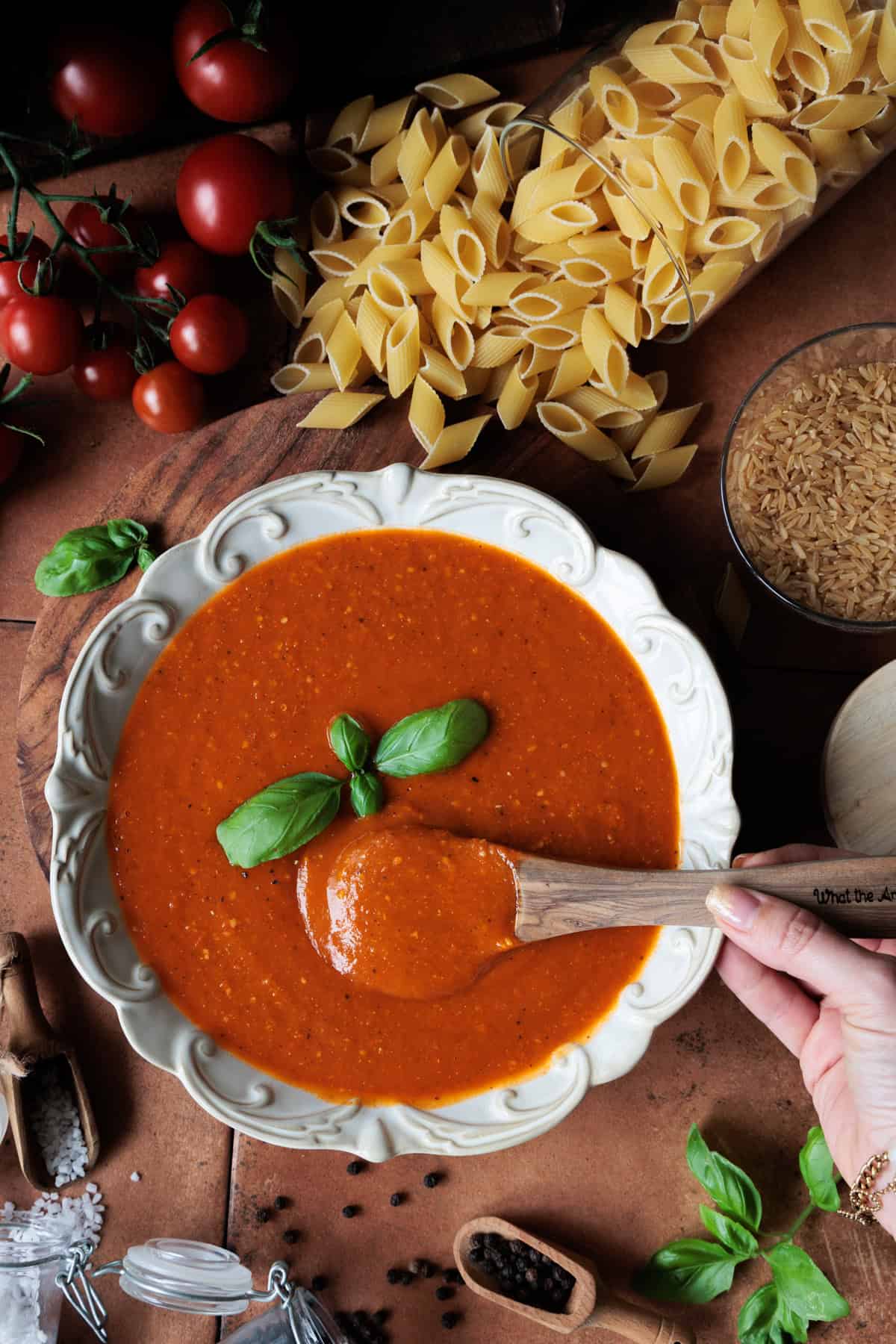 Nur die Tomatensoße in einem Teller mit Verzierungen. Frische Basilikumblätter sind zu sehen sowie im Hintergrund Reis, Nudeln und Salz-sowie Pfefferkörner.