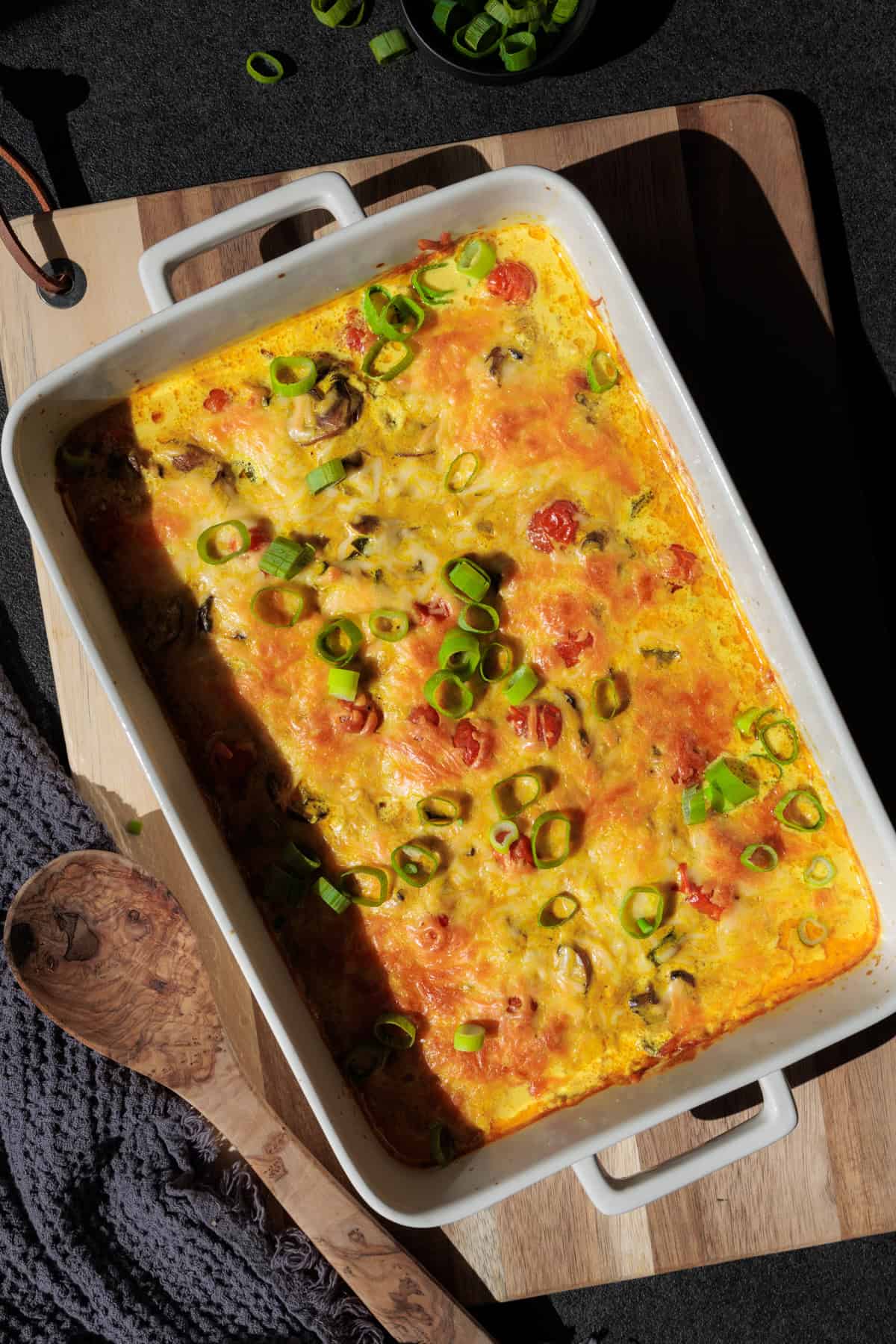 Schnitzel-Gratin in einer Auflaufform auf einem Holztablett. Mit frischen Lauchzwiebeln garniert.