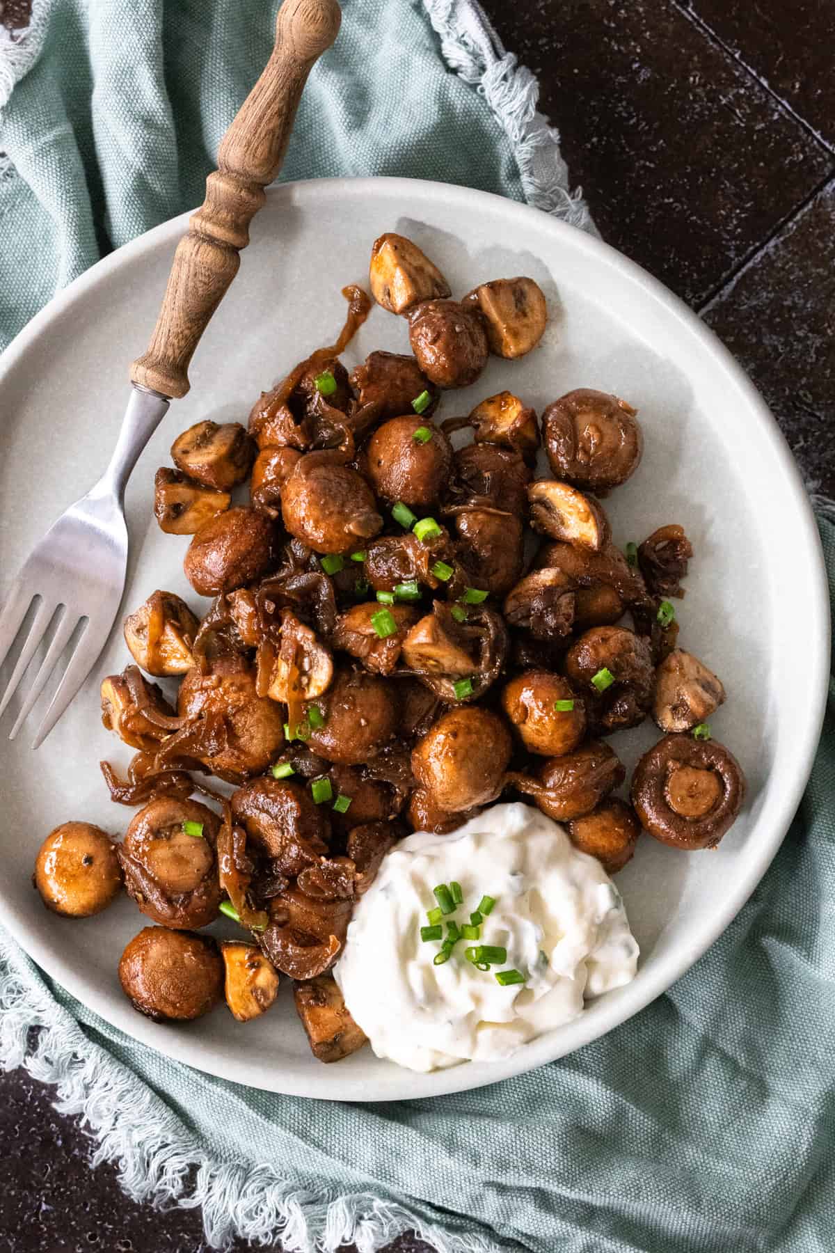 Champignons in Knoblauchsoße auf einem hellen Teller, mit einer Gabel darauf.