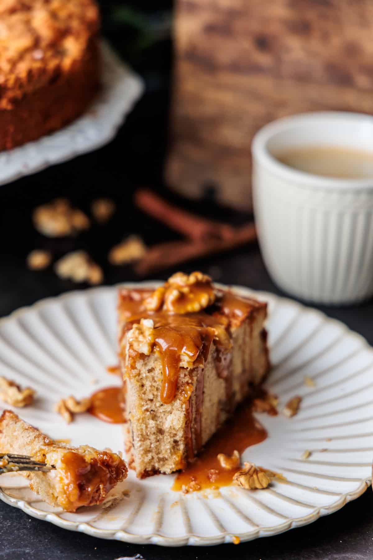 Ein Stück des Weihnachtskuchens mit Apfel und Walnuss auf einem Kuchenteller, Karamellcreme läuft am Kuchenstück hinunter.