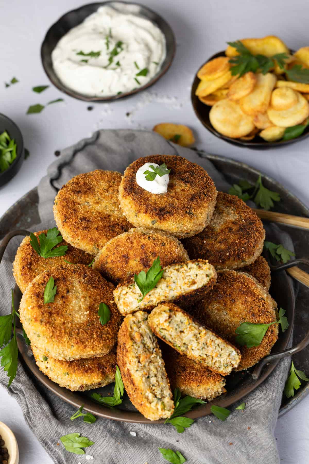 Gemüsefrikadellen (Vegetarische Frikadellen) mit Reis und Quark auf einem Teller, mit viel frischer Petersilie bestreut. Die Frikadelle in der Mitte ist halbiert, sodass man das Innere sehen kann.