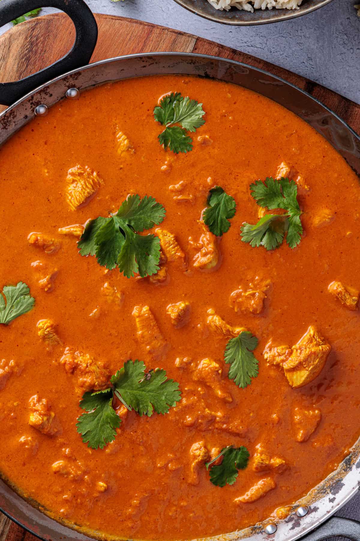 Nahaufnahme des Butter Chicken von oben in die Schüssel fotografiert. Ein paar frische Korianderblätter liegen auf der Soße.