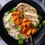 Butter Chicken aus dem Thermomix® in einem schwarzen Teller mit Reis, Naanbrot und frischem Koriander angerichtet.