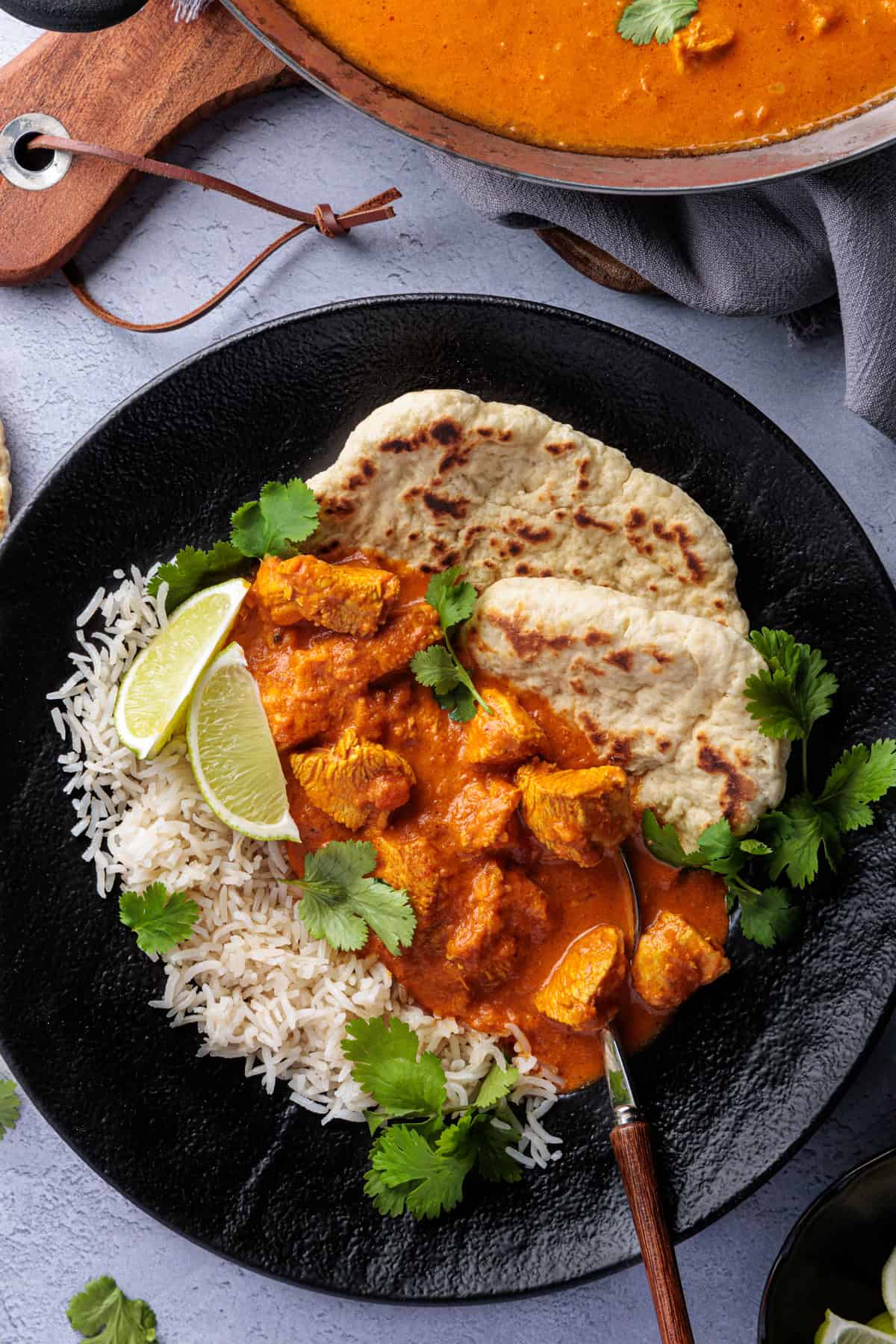 Butter Chicken aus dem Thermomix® in einem schwarzen Teller mit Reis, Naanbrot und frischem Koriander angerichtet.