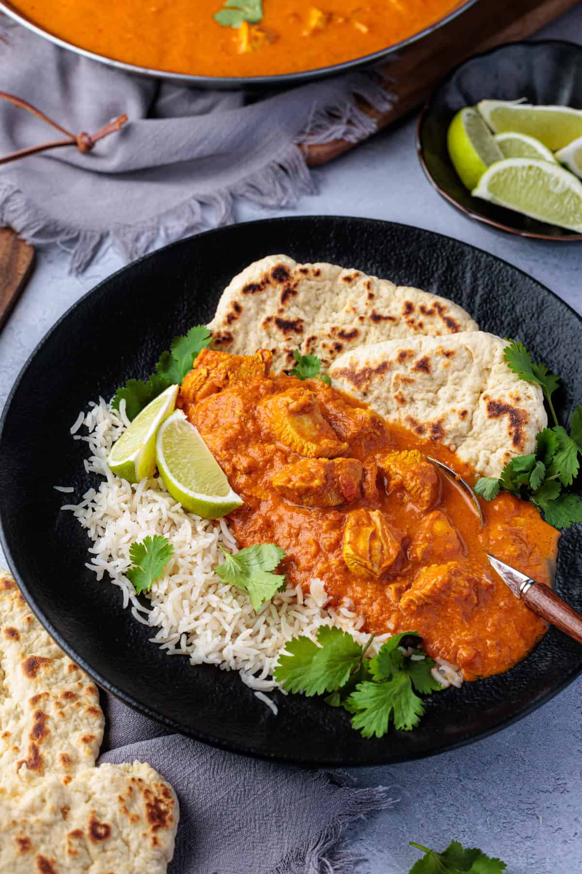 Cremiges, leicht scharfes Butter Chicken aus dem Thermomix® in einem schwarzen Teller mit Reis, Naanbrot und frischem Koriander angerichtet.