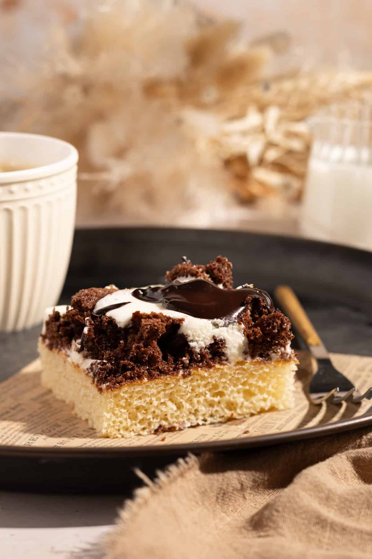 Blechkuchen mit Milchmädchen, Schmand und Kakao (Dalmatiner Kuchen) auf einem Metall-Tablett, seitlich fotografiert. Im Hintergrund Trockenblumen und eine Kaffetasse.