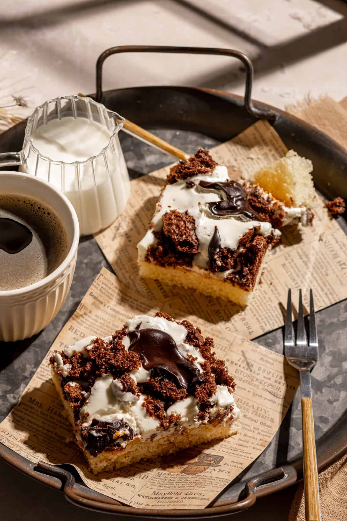 Schokoladen-Blechkuchen mit Milchmädchen-Creme (gezuckerter Kondensmilch) - auch Dalmatiner Kuchen genannt. 2 Kuchenstücke auf einem Tablett. Daneben Kaffee in einer Tasse und ein Milchkännchen.