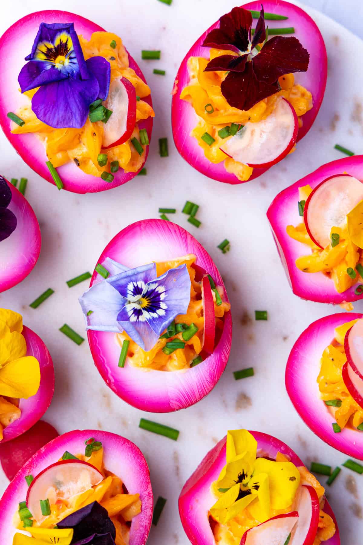 Nahaufnahme von leckeren, gefüllten, gekochten Eiern durch Rote Beete Sud rosa gefärbt, dekoriert mit essbaren Blüten. Auch "Deviled Eggs" genannt, sind ein perfekter Hingucker für dein Osterbuffet. Rezept auch für den Thermomix® geeignet.