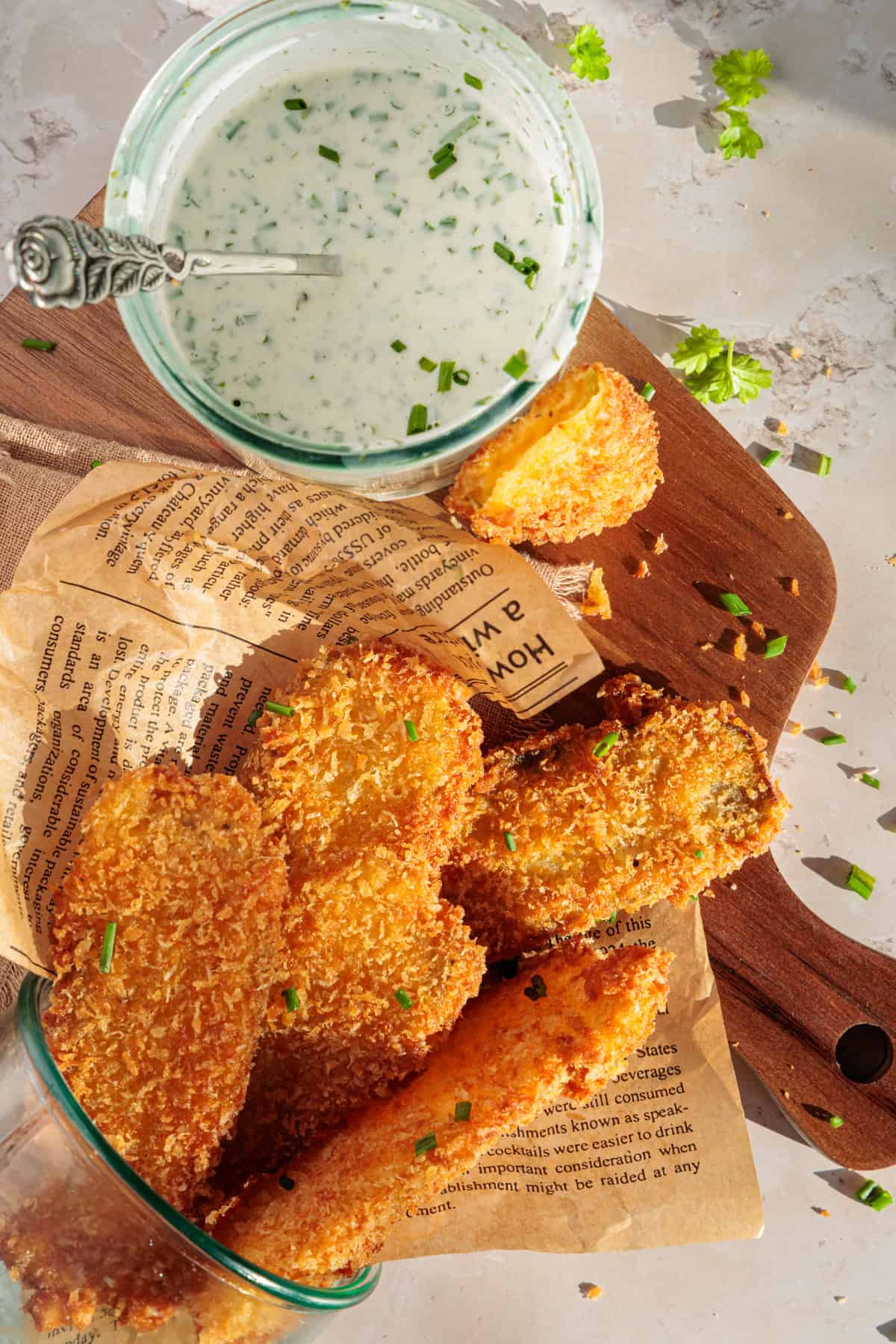 Die Gewürzgurken (paniert und frittiert) liegen in einem umgekippten Glas auf einem Holzbrett. Daneben steht ein Glas mit dem selbstgemachten Ranch-Dip.