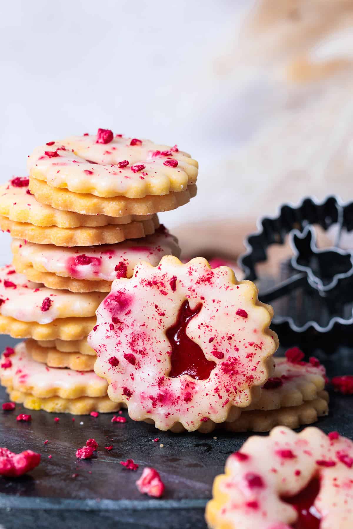 Mürbeteig trifft auf süße Himbeeren: Hausgemachte Osterhasen-Kekse: Ein Stapel selbstgebackener Osterkekse in Form von Hasen. Die goldbraunen Kekse sind mit einer zarten weißen Glasur überzogen und mit roten Himbeerstückchen dekoriert. Im Hintergrund sind Ausstecher in Hasenform zu sehen.