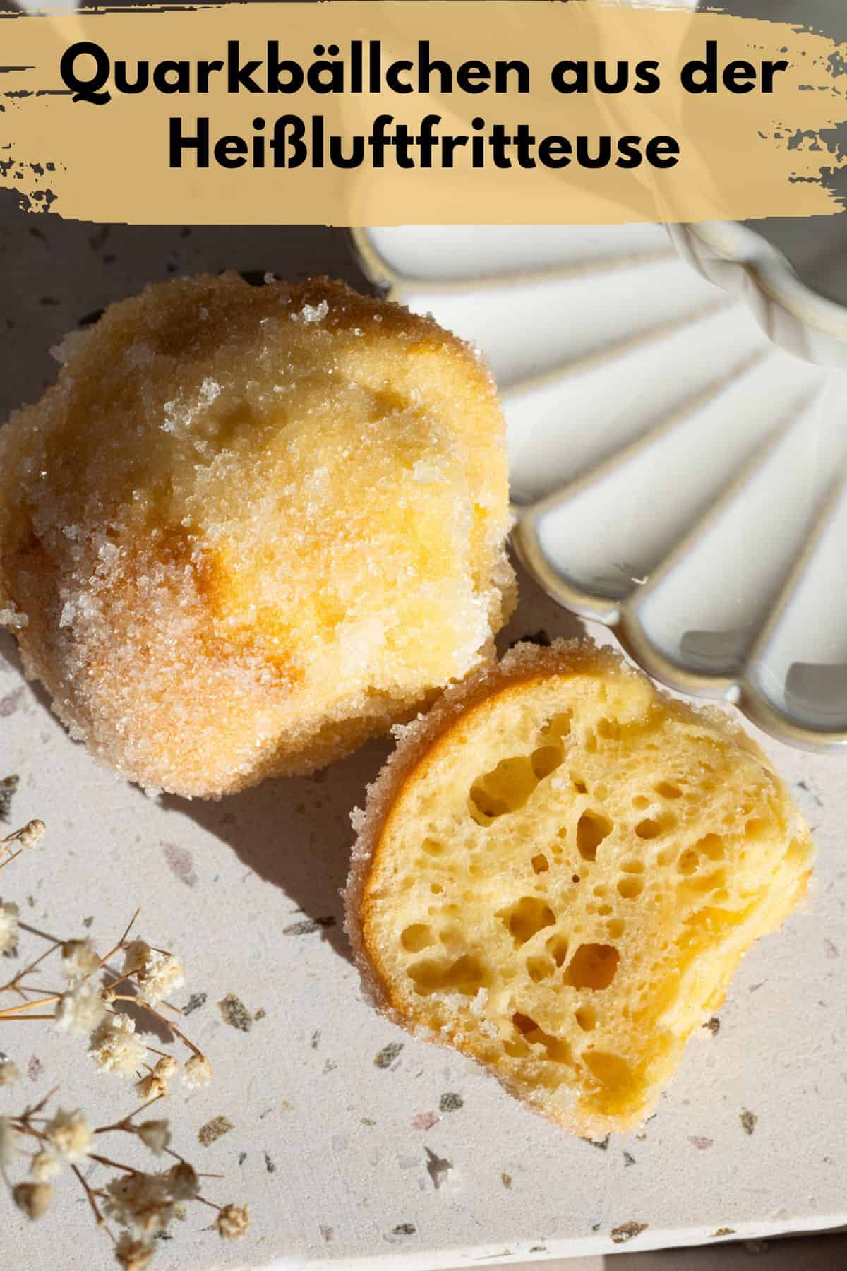 Pin zu Pinterest: Makroaufnahme von zwei Quarkbällchen aus der Heißluftfritteuse, die die poröse und leichte Textur des Inneren und die goldbraune, leicht gezuckerte Oberfläche zeigen. Beide Quarkbällchen liegen auf einem Steinzeug-Brett, daneben ist eine Kaffeetasse mit Untertasse zu erahnen.