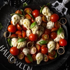 Ein Halloween-Caprese-Salat mit Totenkopf-Mozzarella, Kirschtomaten und gruseliger Deko. Das perfekte schnelle und einfache Rezept für deine Halloween-Party.