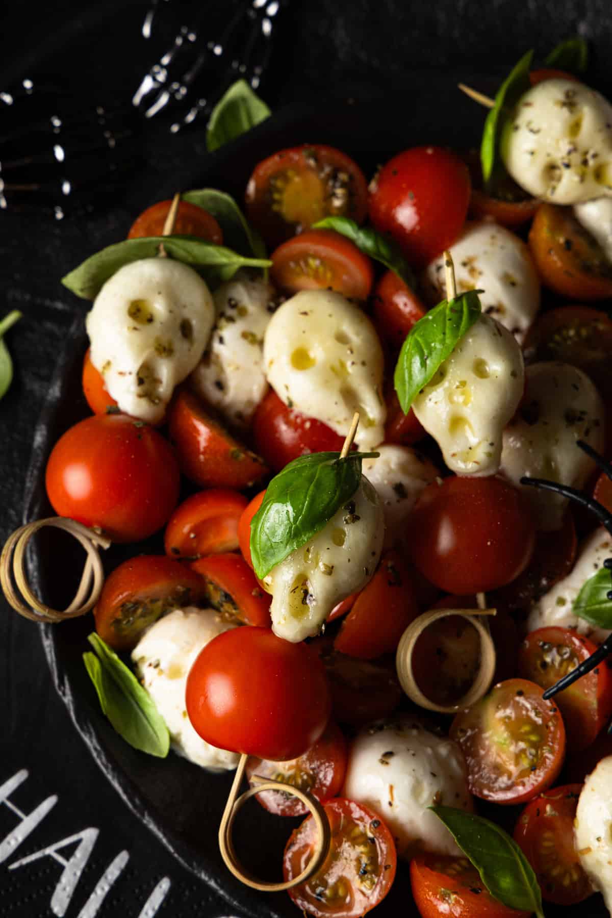 Nahaufnahme eines Halloween-Caprese-Spießes mit einem Mozzarella-Totenknopf, Kirschtomate und Basilikumblatt. Ein schneller und einfacher Halloween-Snack.
